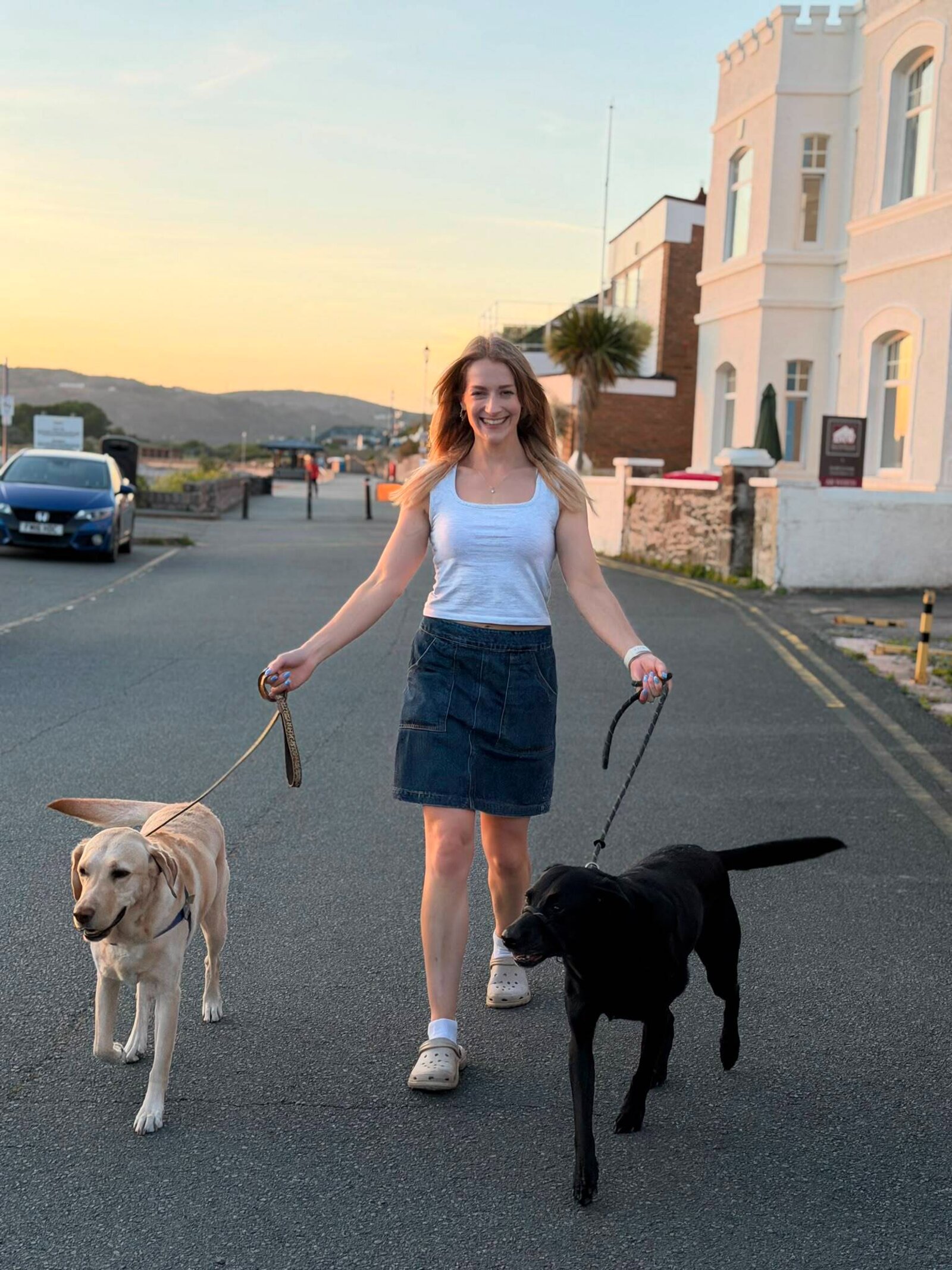 Kathy Brooke walking her two Labradors along a seafront road at sunset